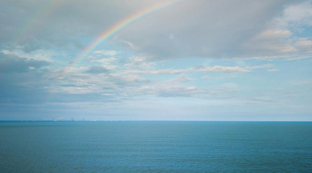 spectacular endless sea against cloudy blue sky with rainbow